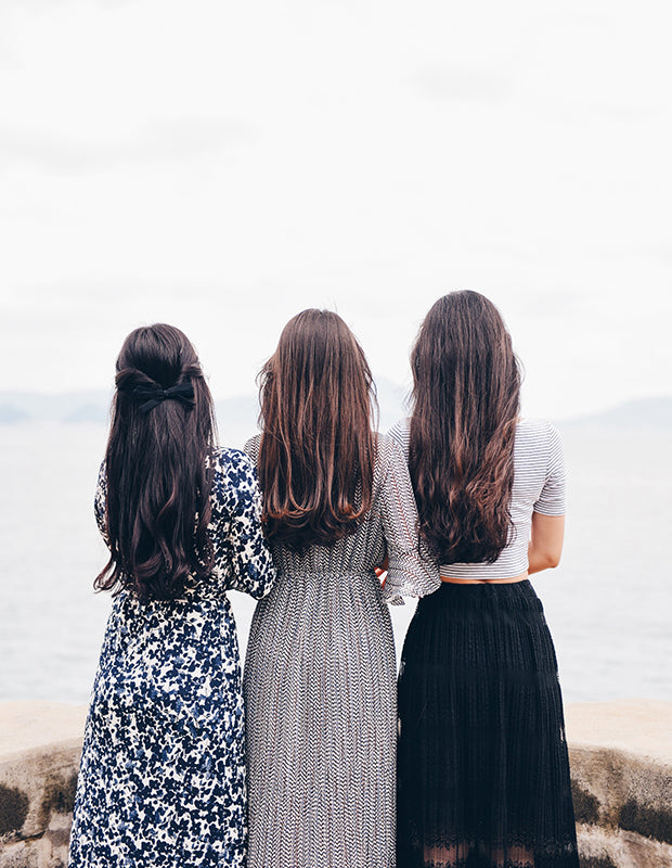 three women facing away, all with long wavy and dark hair