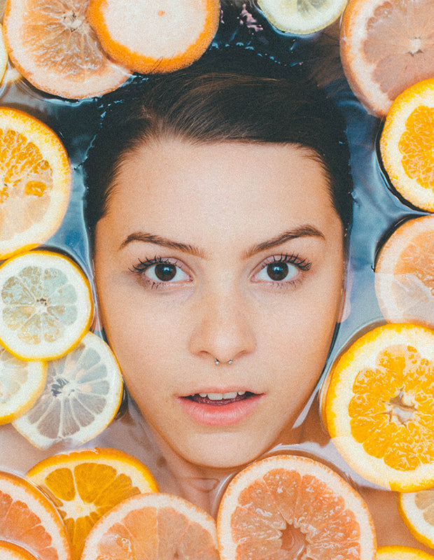 woman's face surrounded by citrus fruits in water