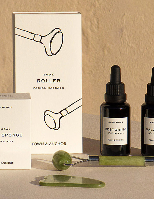 Town & Anchor skincare products and tools on a warmly lit table with textured wall behind