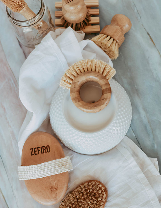 wooden, sustainable brushes for cleaning and beauty arranged on a white marble counter with towels and glass jars