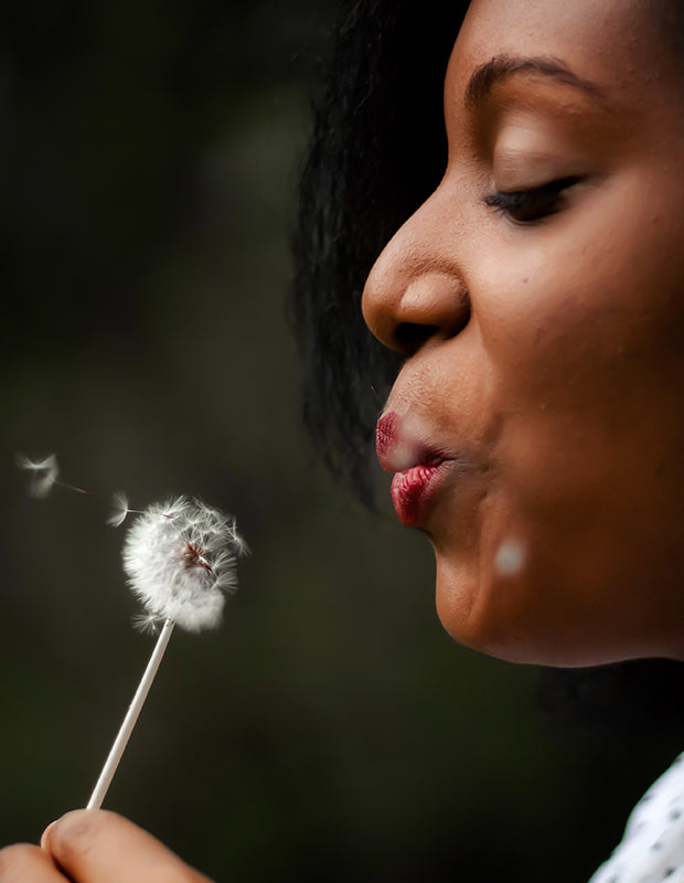 a Black woman blowing a dandelion puff into the wind