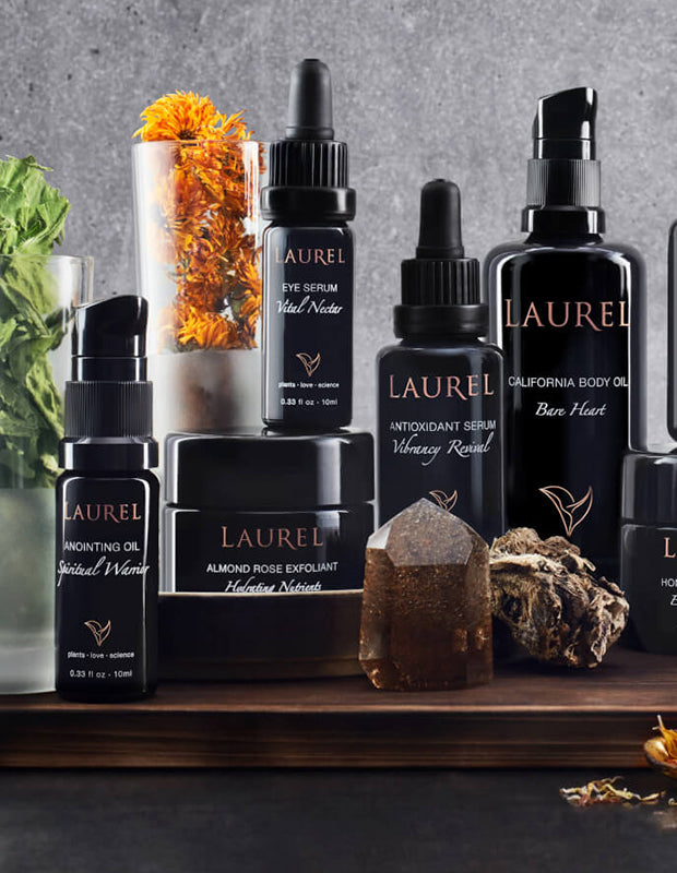 Laurel skincare products in black jars and bottles, arranging nicely on a dark wooden tray, fresh flowers and herbs scattered around