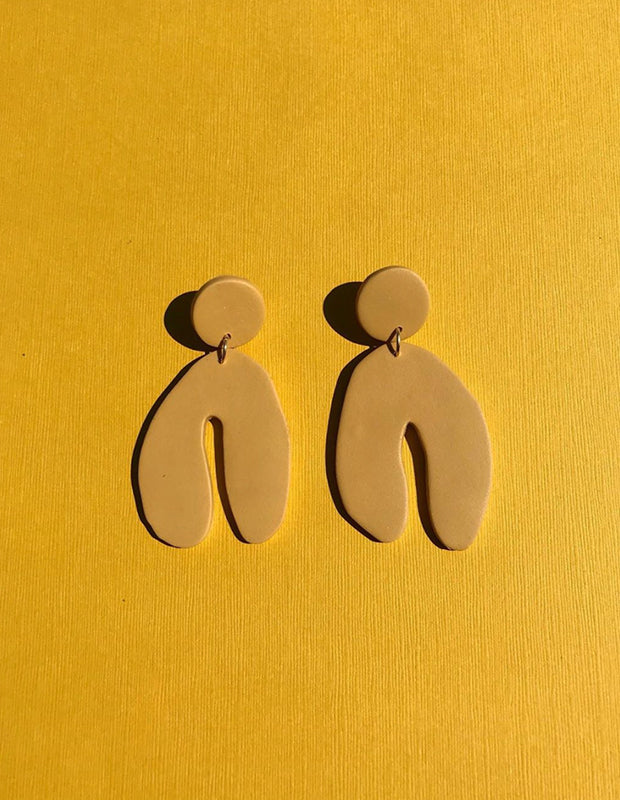 warm yellow polymer earrings sit on a bright yellow cloth background