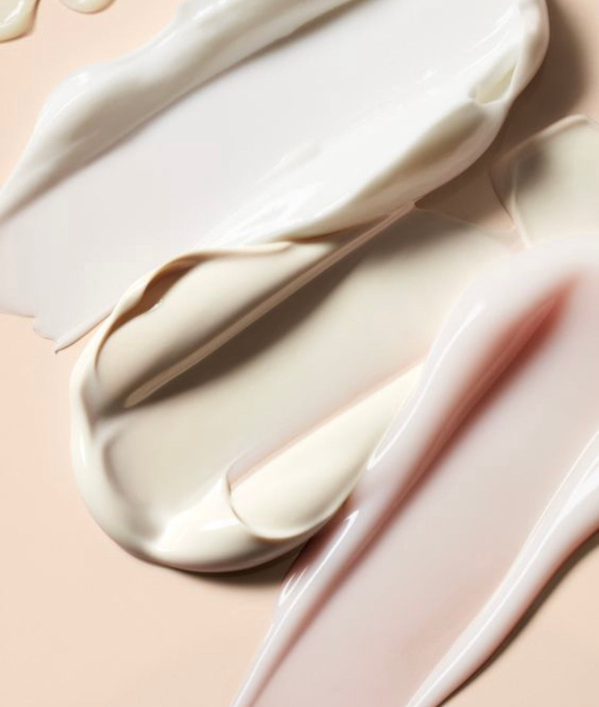 Swirled swatches of ivory and pale pink face cream on a blush background