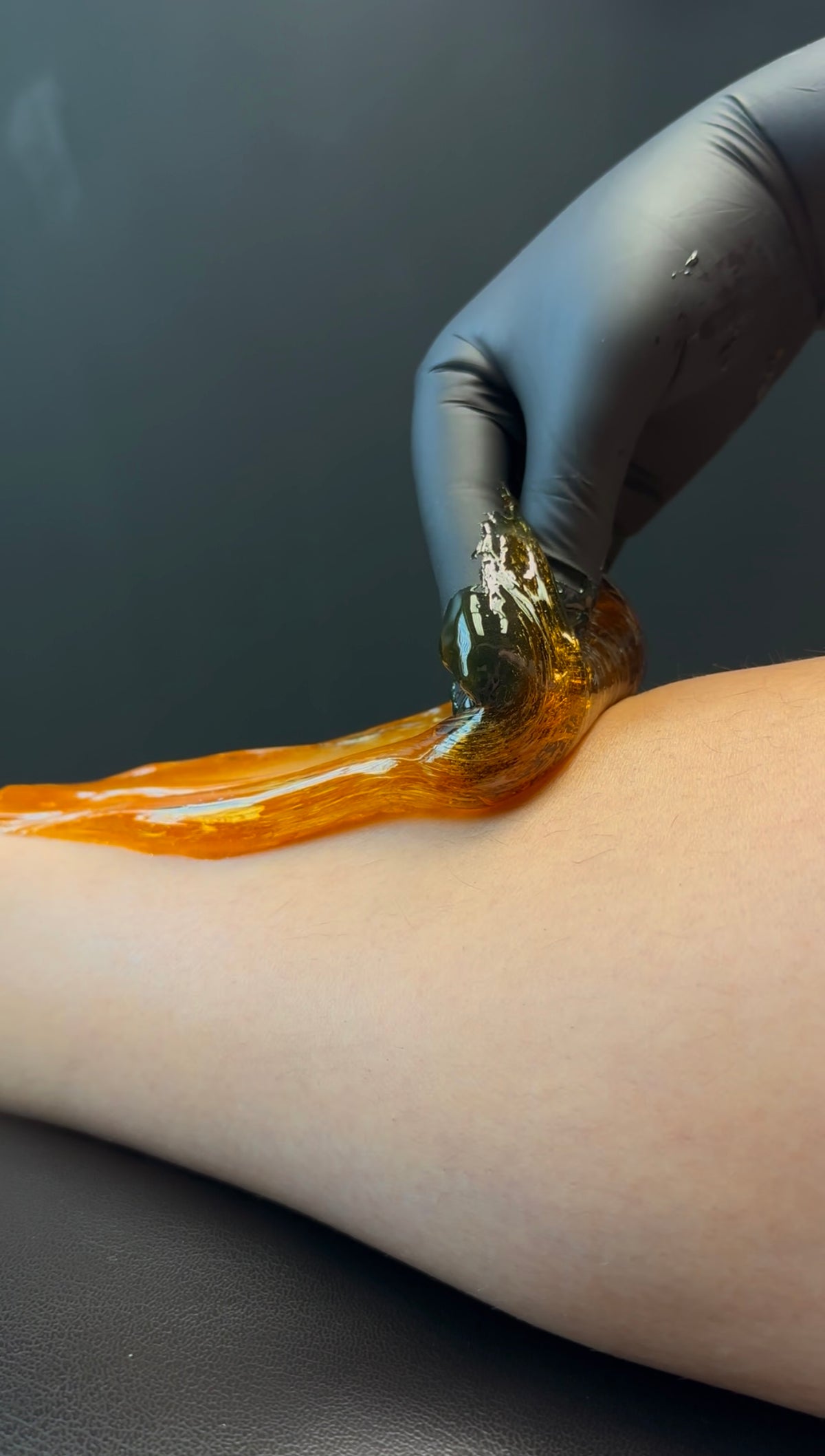 A gloved hand works warm sugaring paste along a client's forearm at Lena Rose.